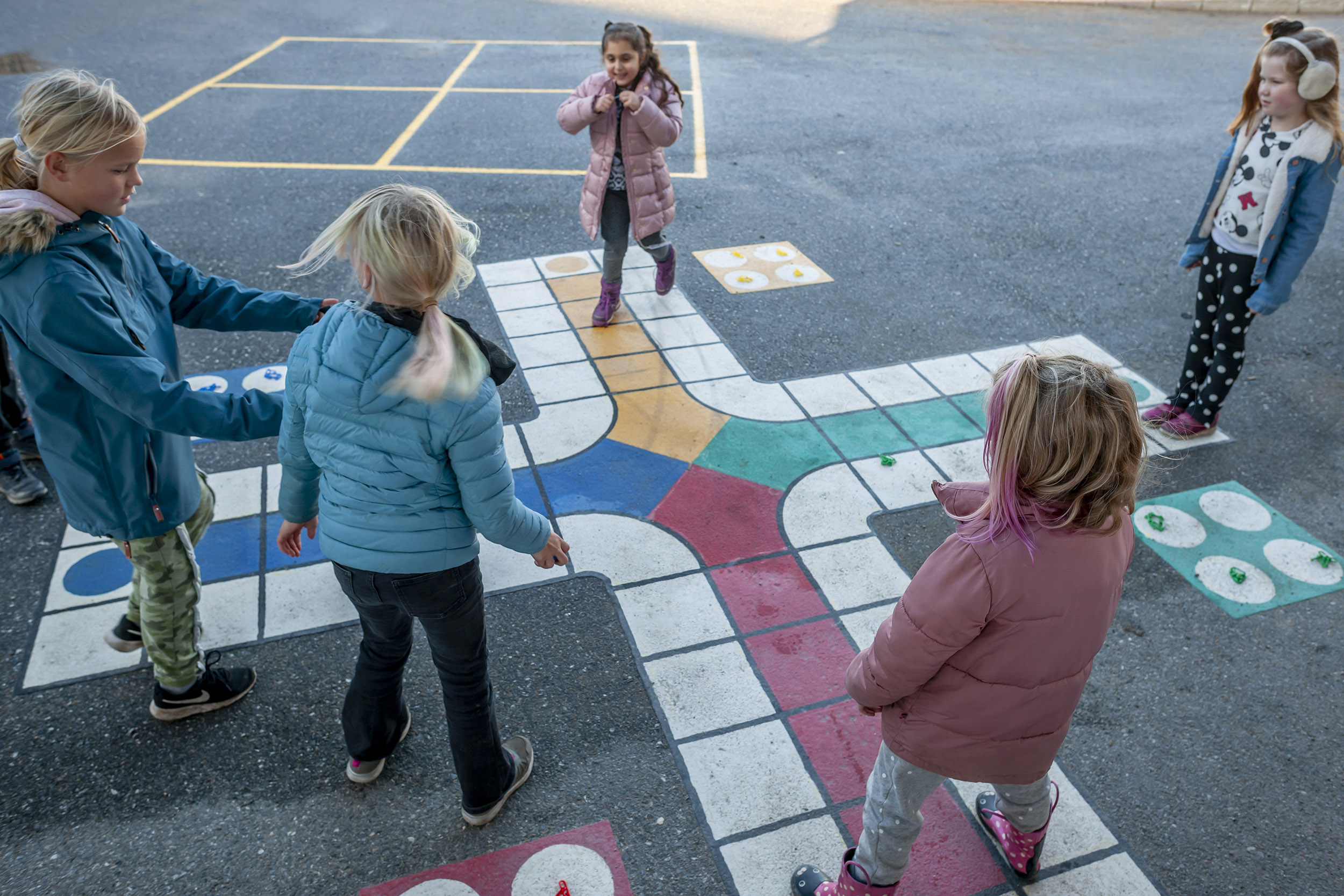 barn lærer i skolegård på oppmerket asfalt formet som ludo-spill.